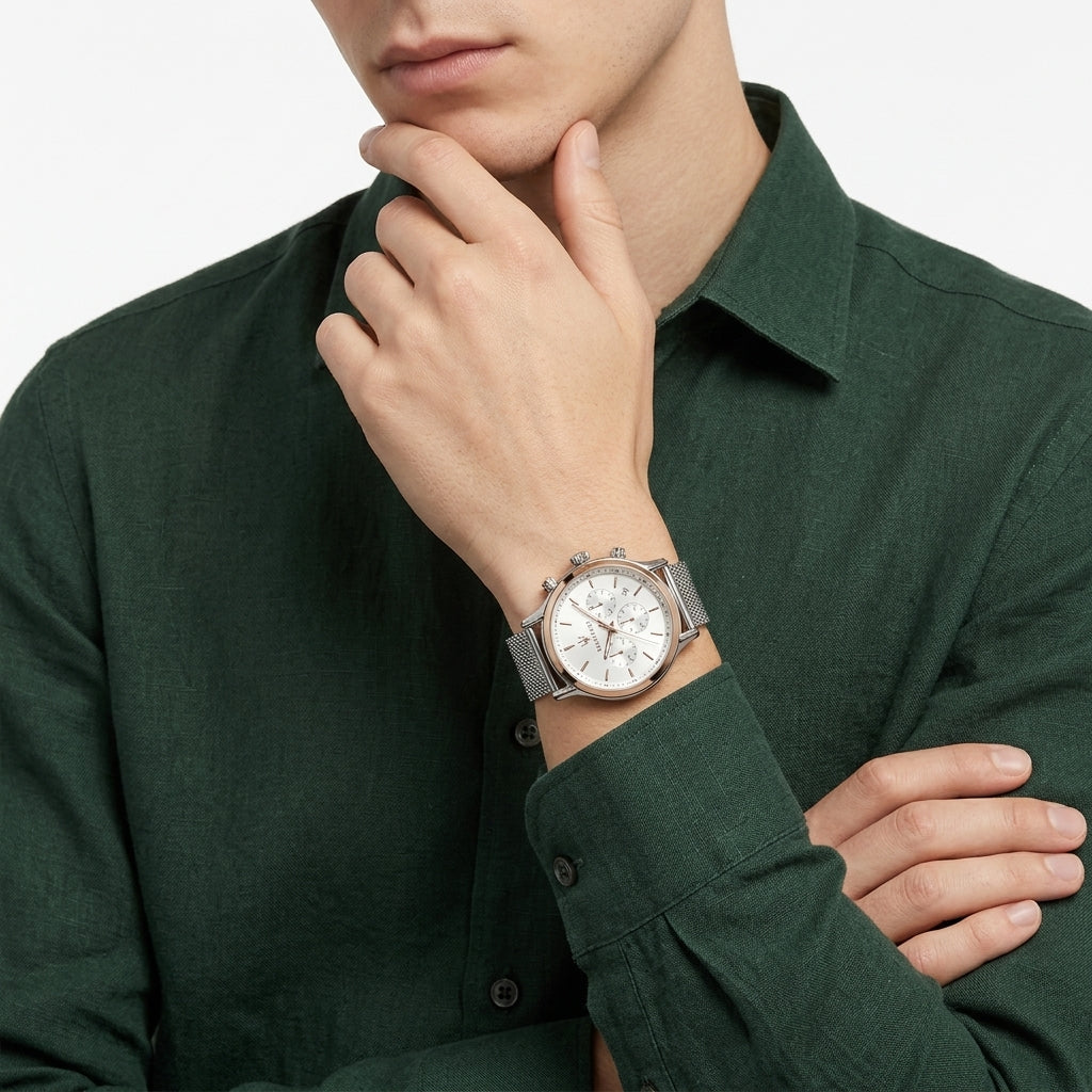 A close-up of a man wearing a dark green linen shirt and a silver-toned chronograph watch with a white dial, resting his chin on his hand.