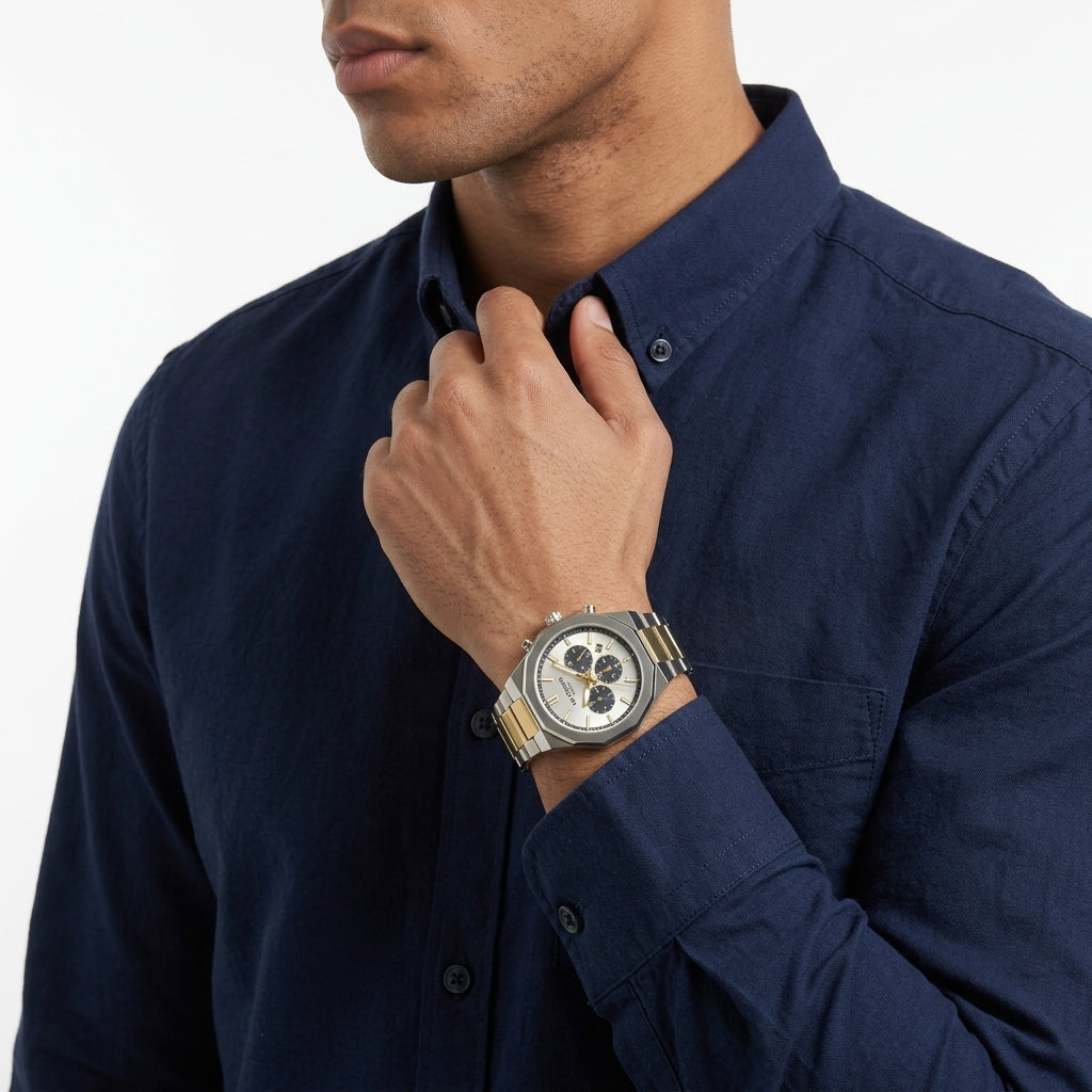 A close-up of a man wearing a navy blue button-down shirt and a silver-toned multi-dial wristwatch with a metal link bracelet, adjusting his collar against a clean white background.