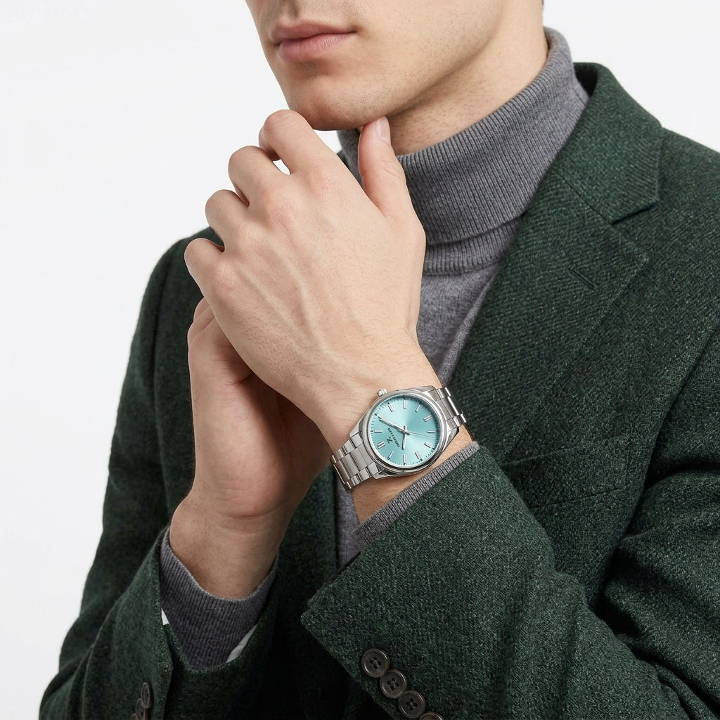 A close-up of a man wearing a silver-toned metal watch with a light blue dial, styled with a gray turtleneck sweater and a dark green textured blazer.
