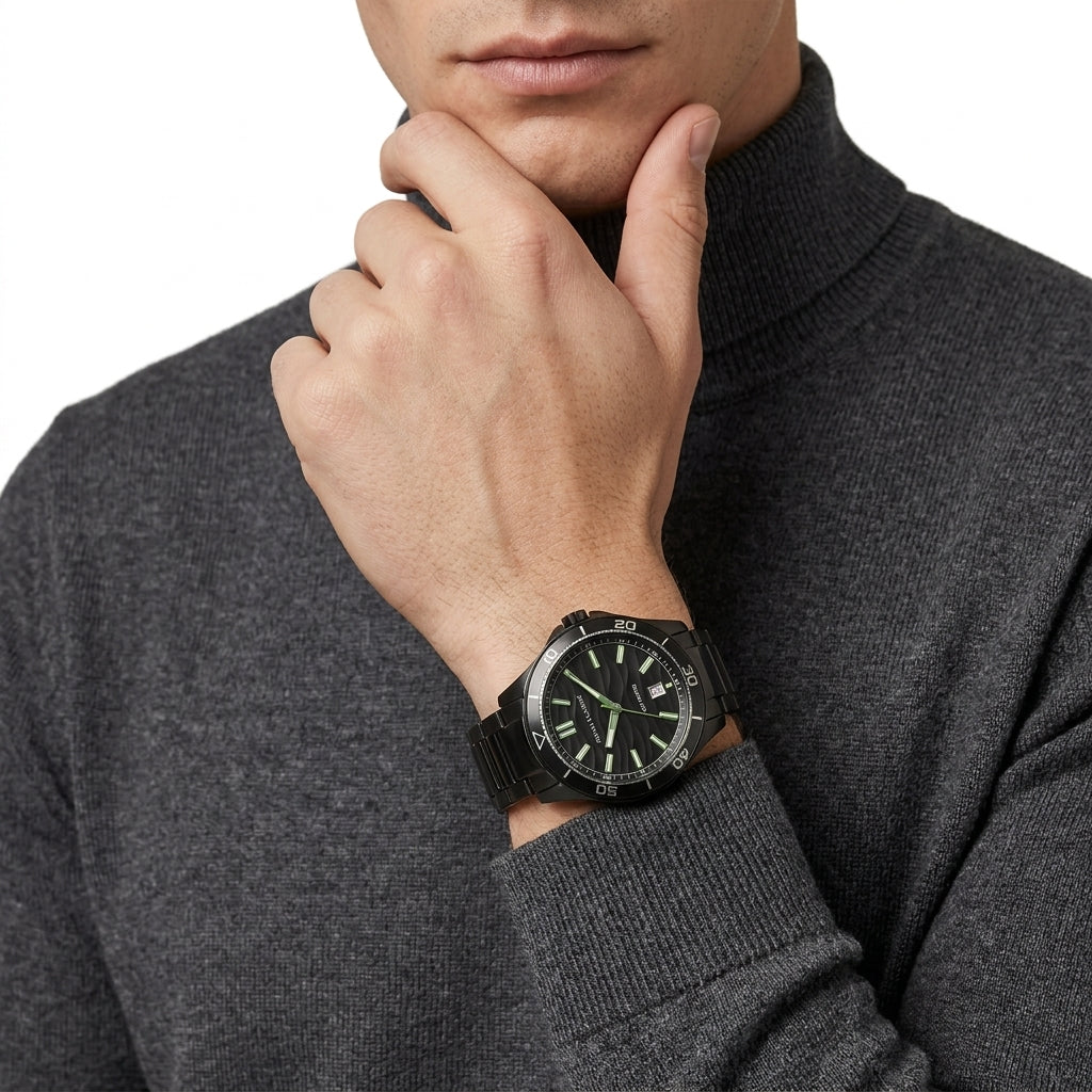 A close-up of a man wearing a black military-style wristwatch with a black dial and matching black strap, styled with a dark gray turtleneck sweater against a white background.