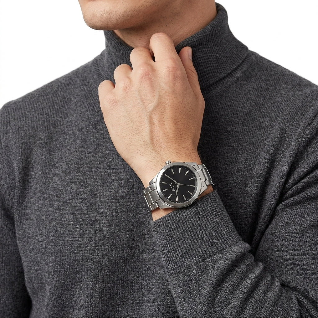 A silver stainless steel wristwatch with a black dial and baton indices, worn on the wrist of a man wearing a dark gray knit turtleneck sweater.