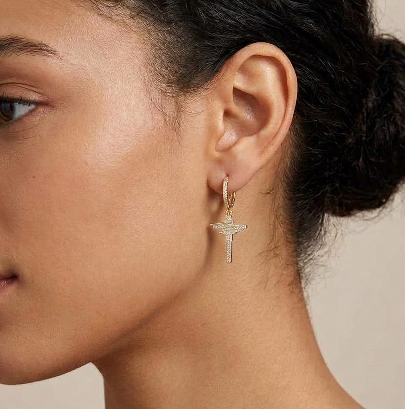 Gold dangle hoop cross earring worn on ear, side profile view