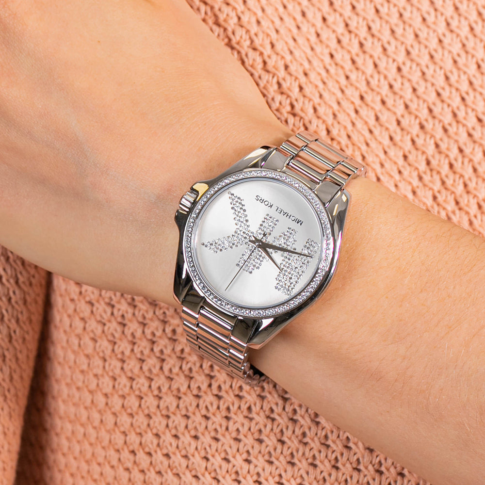 Michael Kors Bradshaw silver-tone watch worn on wrist against peach-colored textile
