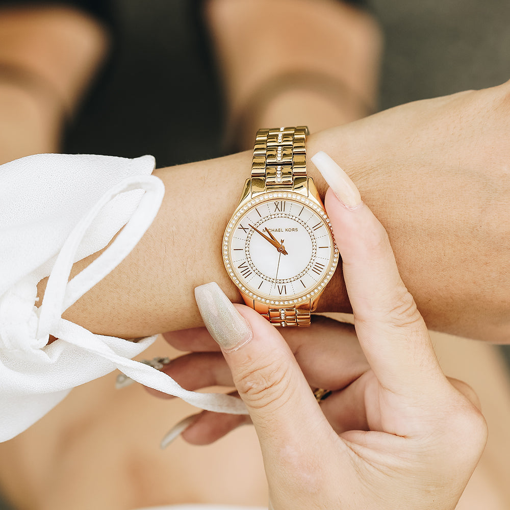 Michael Kors Lauryn gold watch worn on wrist with white dial and Roman numeral markers