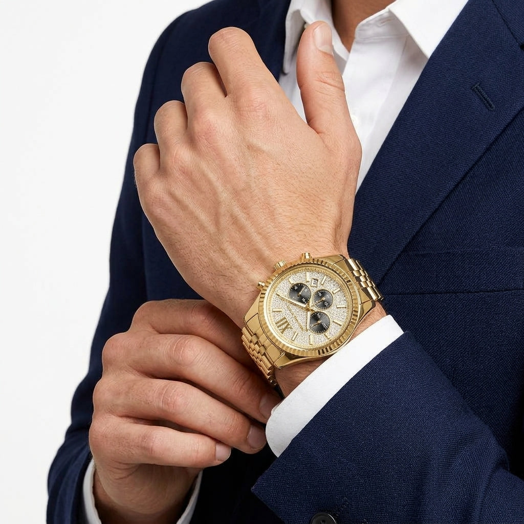 A gold-tone chronograph watch with a white dial and gold link bracelet, shown worn on a man's wrist as he adjusts his navy blue suit jacket and white dress shirt.