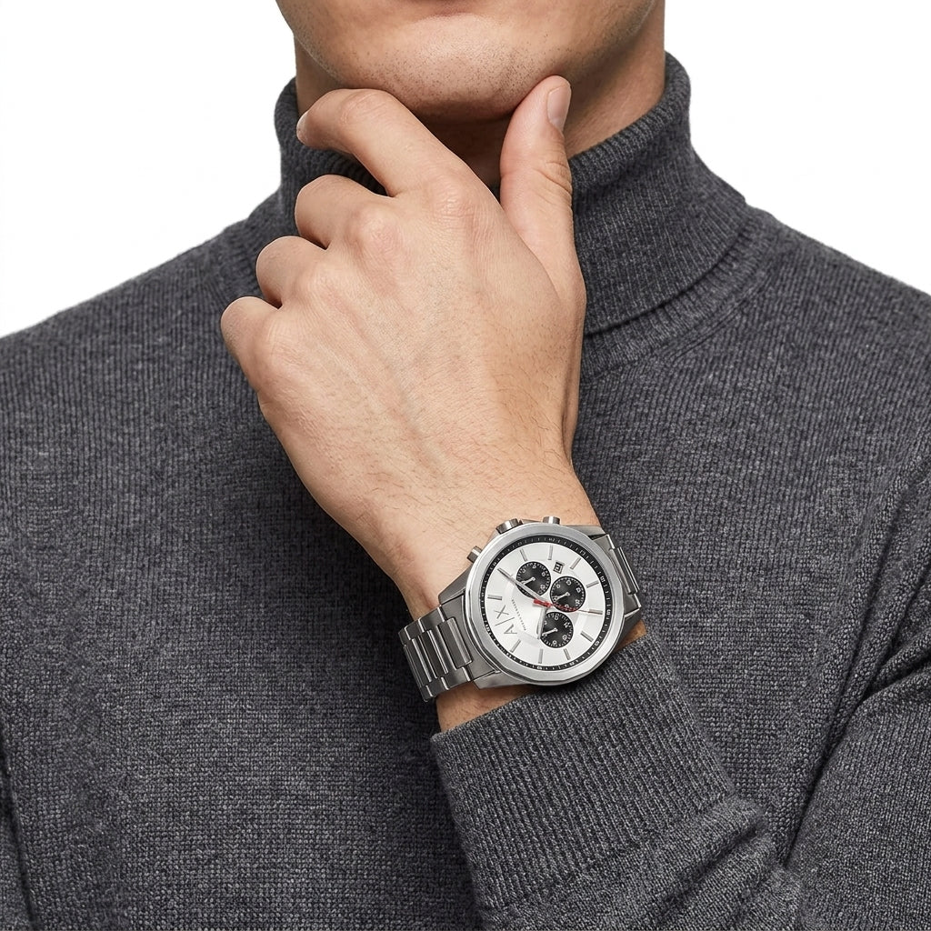 A silver stainless steel wristwatch with a white dial and black sub-dials, worn on the wrist of a man wearing a dark gray turtleneck sweater.