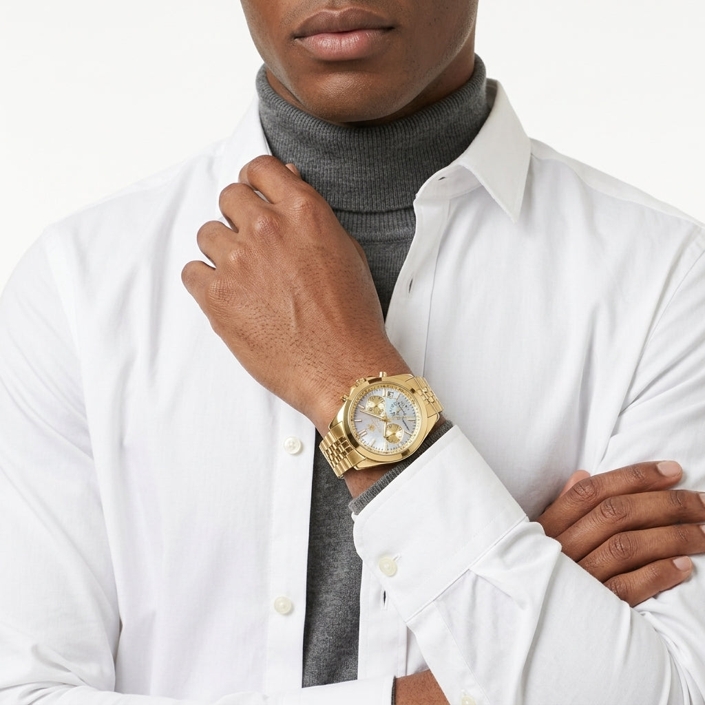 A close-up of a man wearing a gold-tone wristwatch with a white dial, styled with a white dress shirt and a gray turtleneck sweater against a clean white background.